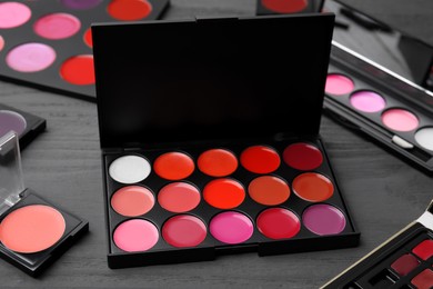 Photo of Colorful lipstick palettes on black wooden table. Professional cosmetics