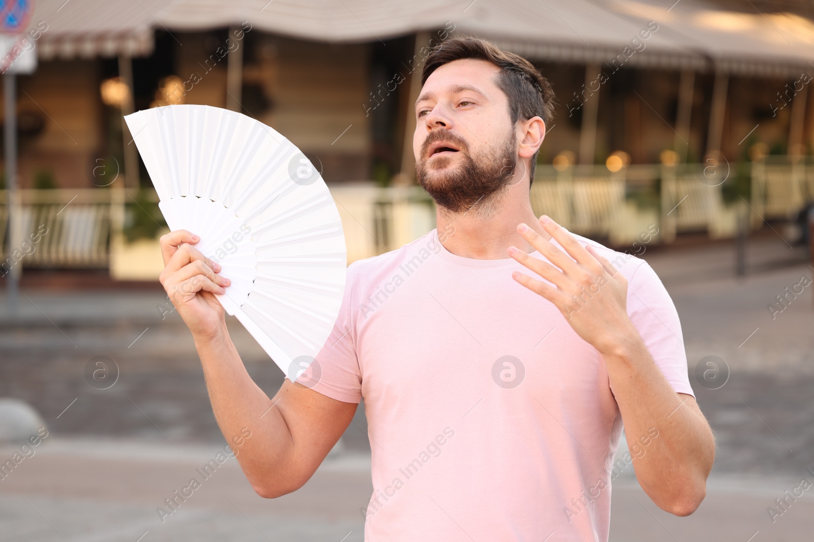 Photo of Man with hand fan suffering from heat outdoors