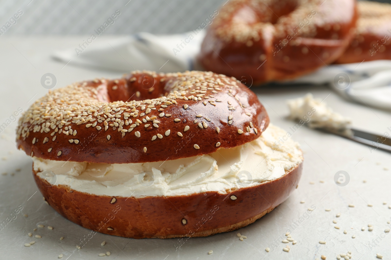 Photo of Delicious bagel with cream cheese on light table, closeup