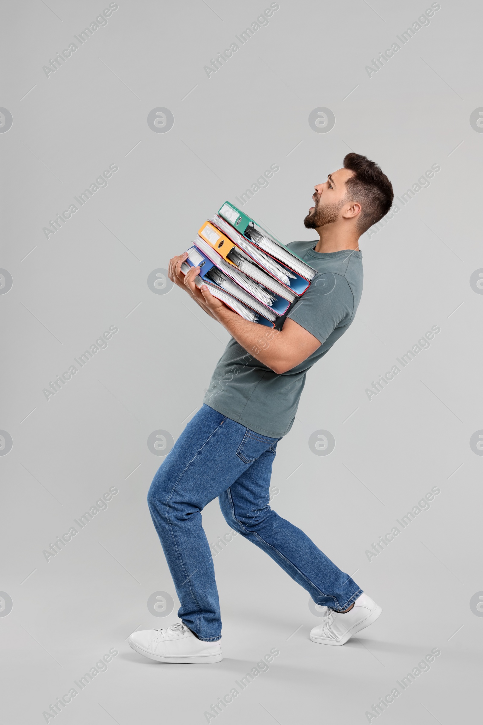 Photo of Stressful man with folders walking on light gray background