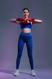 Photo of Beautiful woman wearing boxing gloves in color lights on grey background