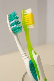 Photo of New toothbrushes in glass holder on blurred background, closeup