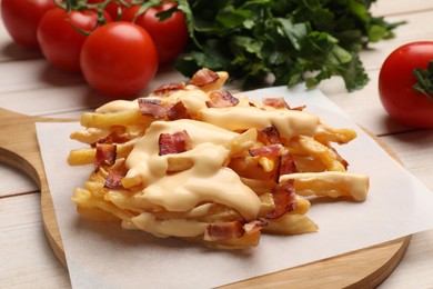 Photo of Delicious French fries with bacon, cheese sauce, tomatoes and herbs on wooden table, closeup