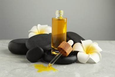 Photo of Bottle of face serum with spa stones and beautiful flowers on light grey table