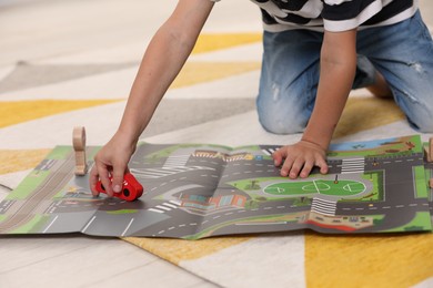 Photo of Little boy playing with set of wooden road signs and cars indoors, closeup. Child's toy