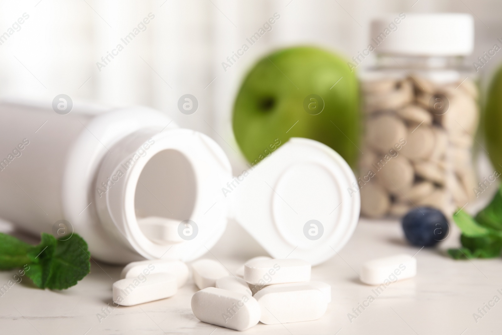 Photo of Bottle with vitamin pills and mint on light table, closeup
