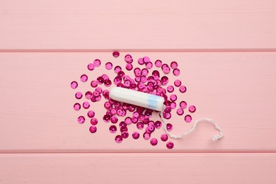 Tampon and sequins on pink wooden background, flat lay. Menstrual hygiene product