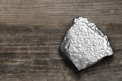 Photo of One silver nugget on wooden table, top view. Space for text