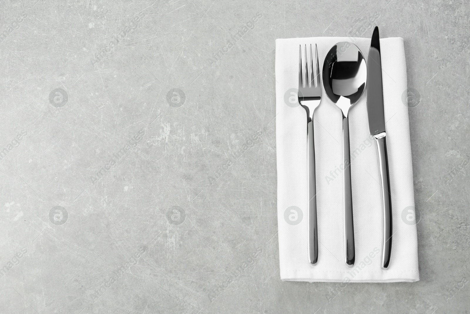 Photo of Stylish cutlery set and napkin on grey table, top view. Space for text