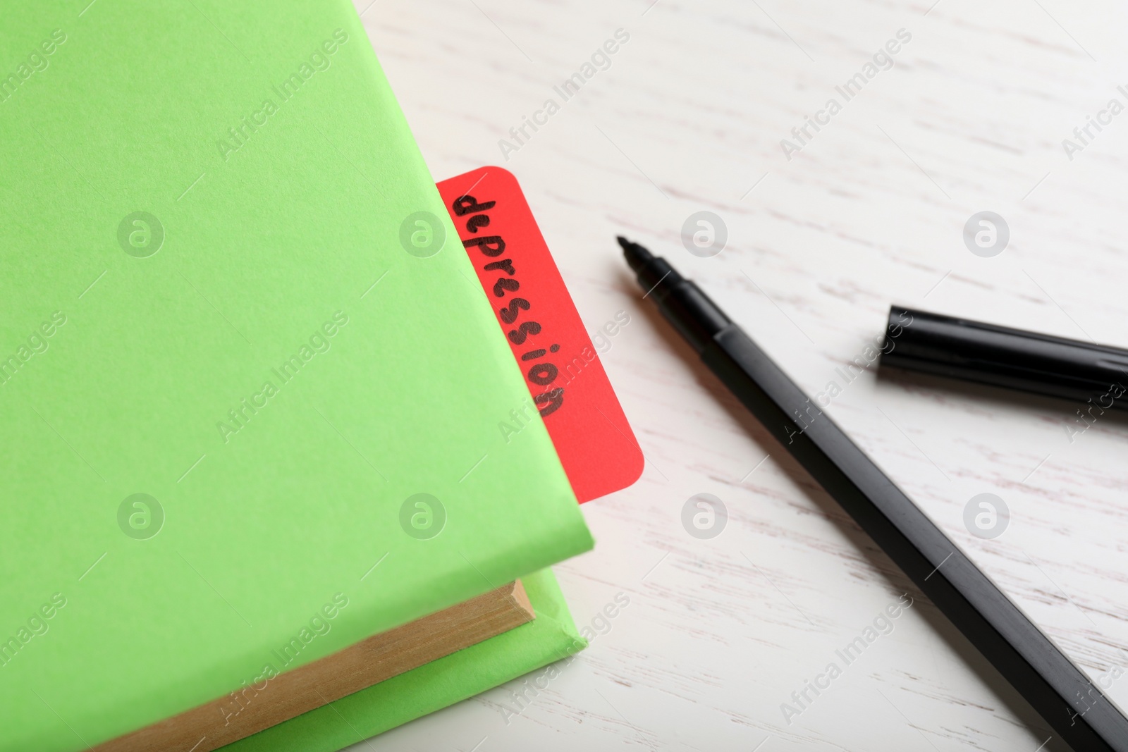 Photo of Note with word Depression in book and black felt tip pen on white wooden table, closeup