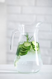 Photo of Refreshing cucumber water with rosemary in jug on white table against brick wall