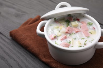 Delicious cold summer soup (okroshka) with boiled sausage in pot on grey wooden table, closeup. Space for text