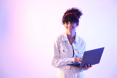 Photo of Beautiful young woman with laptop on color background in neon lights. Space for text