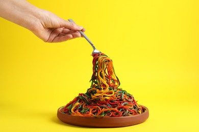 Photo of Woman eating delicious spaghetti painted with different food colorings on yellow background, closeup