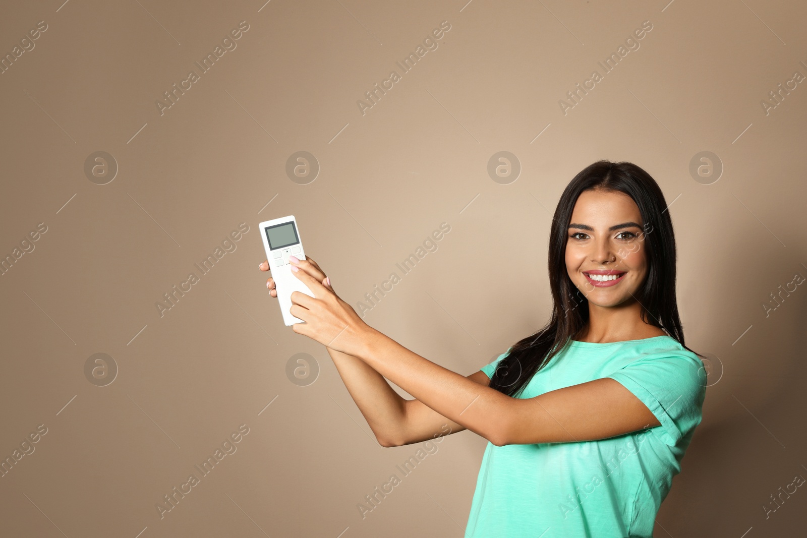 Photo of Young woman with air conditioner remote on beige background. Space for text