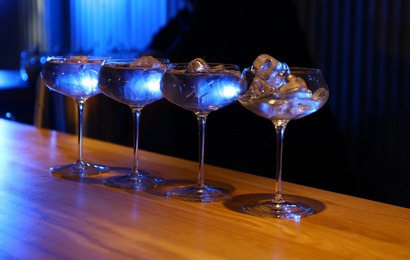Photo of Glasses of vodka with ice cubes on wooden counter in bar
