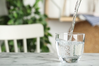 Photo of Pouring water into glass on white marble table indoors, space for text. Refreshing drink
