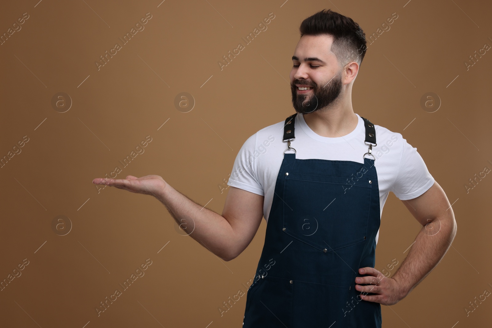 Photo of Smiling man in kitchen apron holding something on brown background. Mockup for design