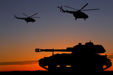 Silhouettes of army tank and helicopters at sunset outdoors. Military machinery 