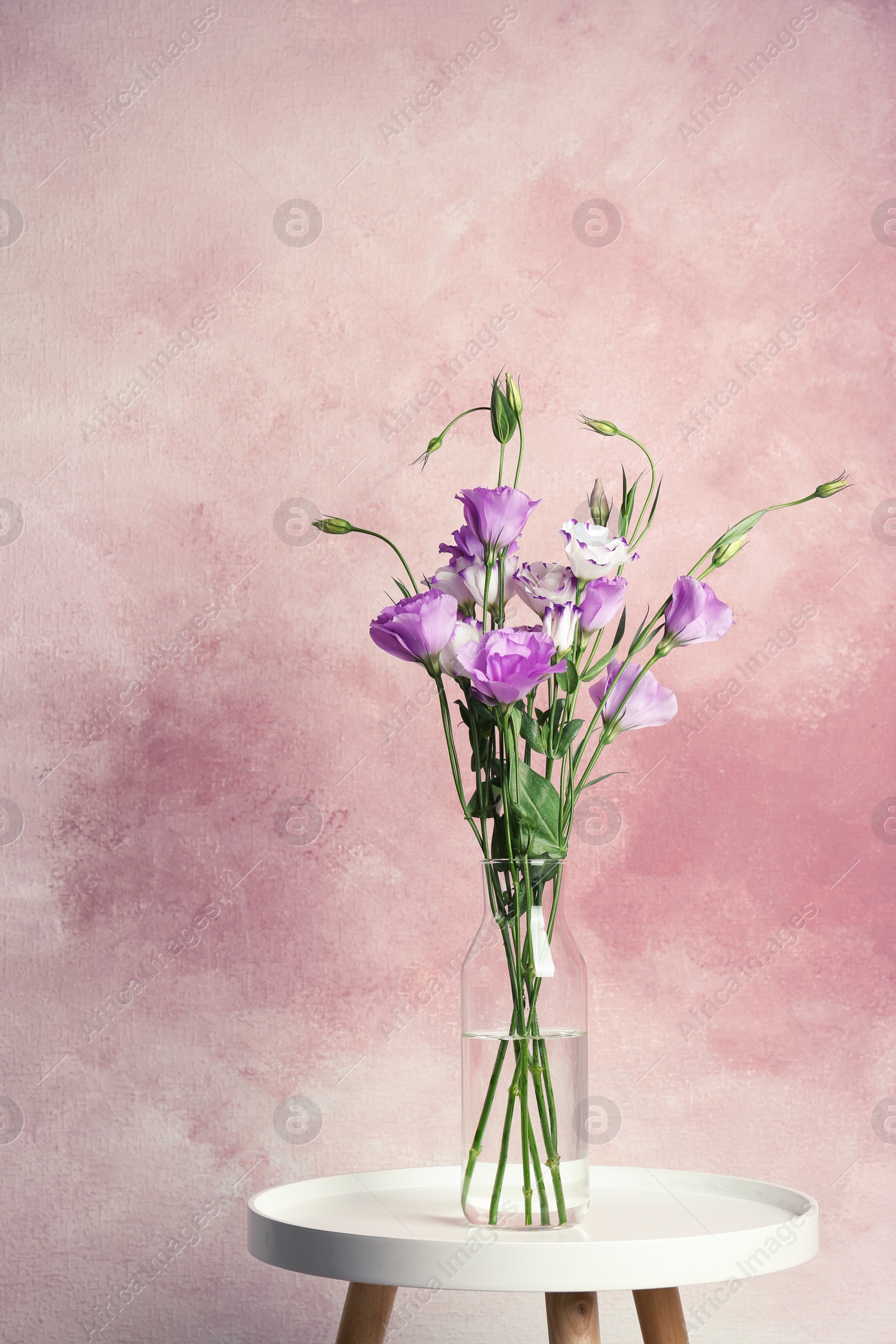 Photo of Vase with bouquet of beautiful flowers on table against color background