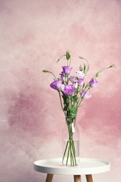 Photo of Vase with bouquet of beautiful flowers on table against color background