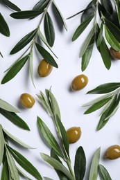 Twigs with olives and fresh green leaves on white background, flat lay