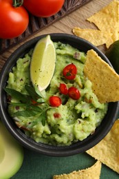 Photo of Delicious guacamole with nachos chips and ingredients on table, flat lay