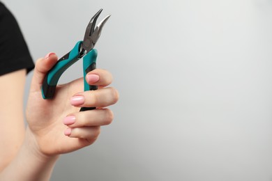 Photo of Woman with bent nose pliers on grey background, closeup. Space for text