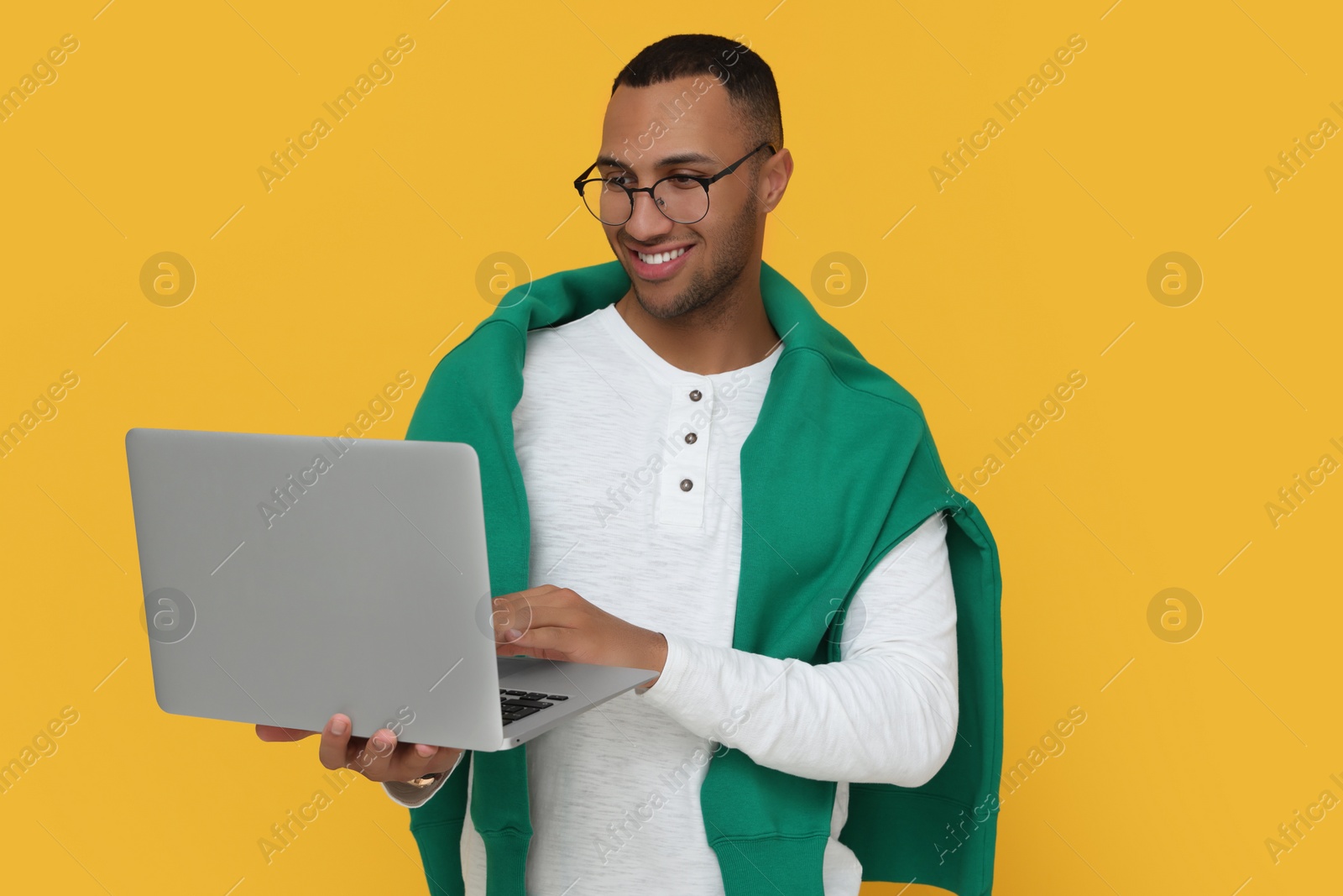 Photo of Happy young intern holding laptop on orange background