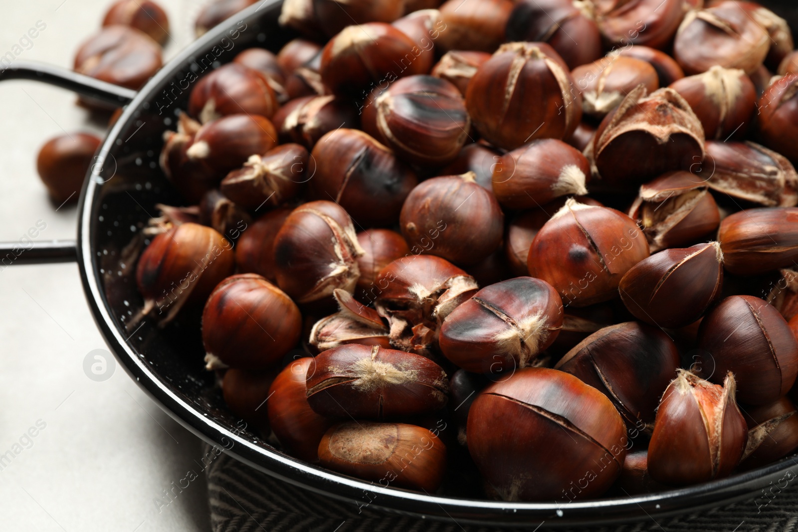 Photo of Delicious roasted edible chestnuts in frying pan on table, closeup