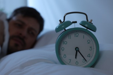 Sleepy man awaking at home in morning, focus on alarm clock. Space for text