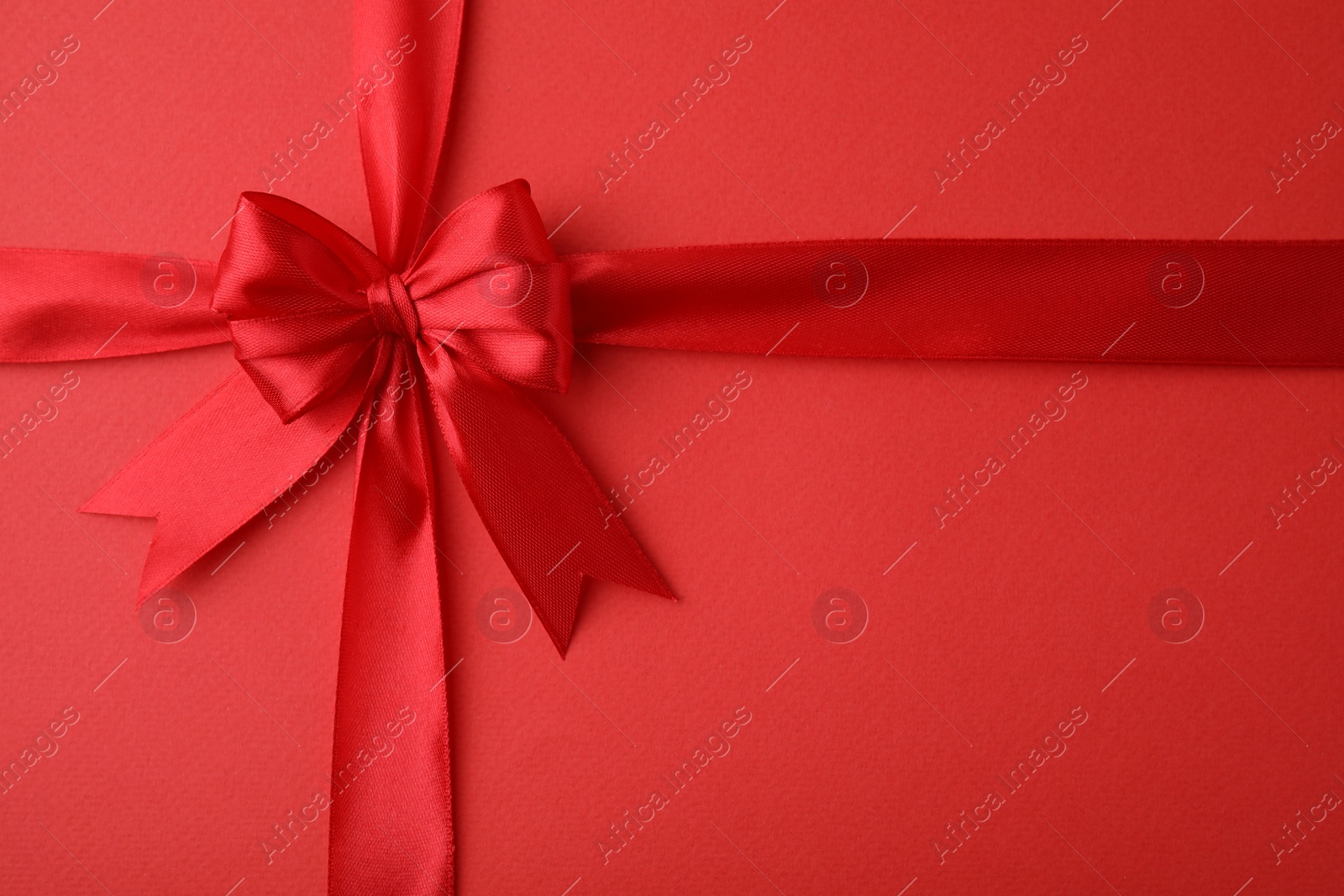 Photo of Bright satin ribbon with bow on red background, top view