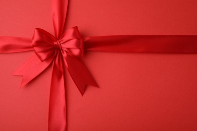 Photo of Bright satin ribbon with bow on red background, top view