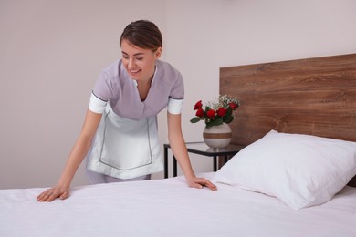 Beautiful chambermaid making bed in hotel room