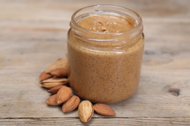 Tasty nut paste in jar and almonds on wooden table, closeup