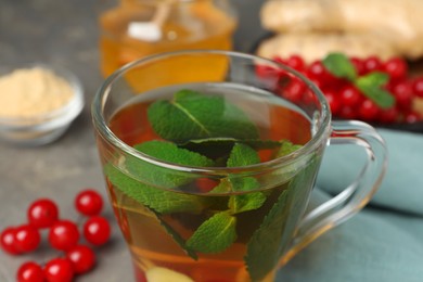 Photo of Glass cup of immunity boosting drink and ingredients on grey table, closeup