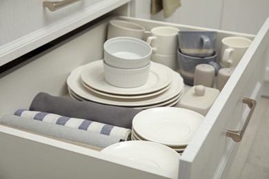 Photo of Open drawer of kitchen cabinet with different dishware and towels, closeup