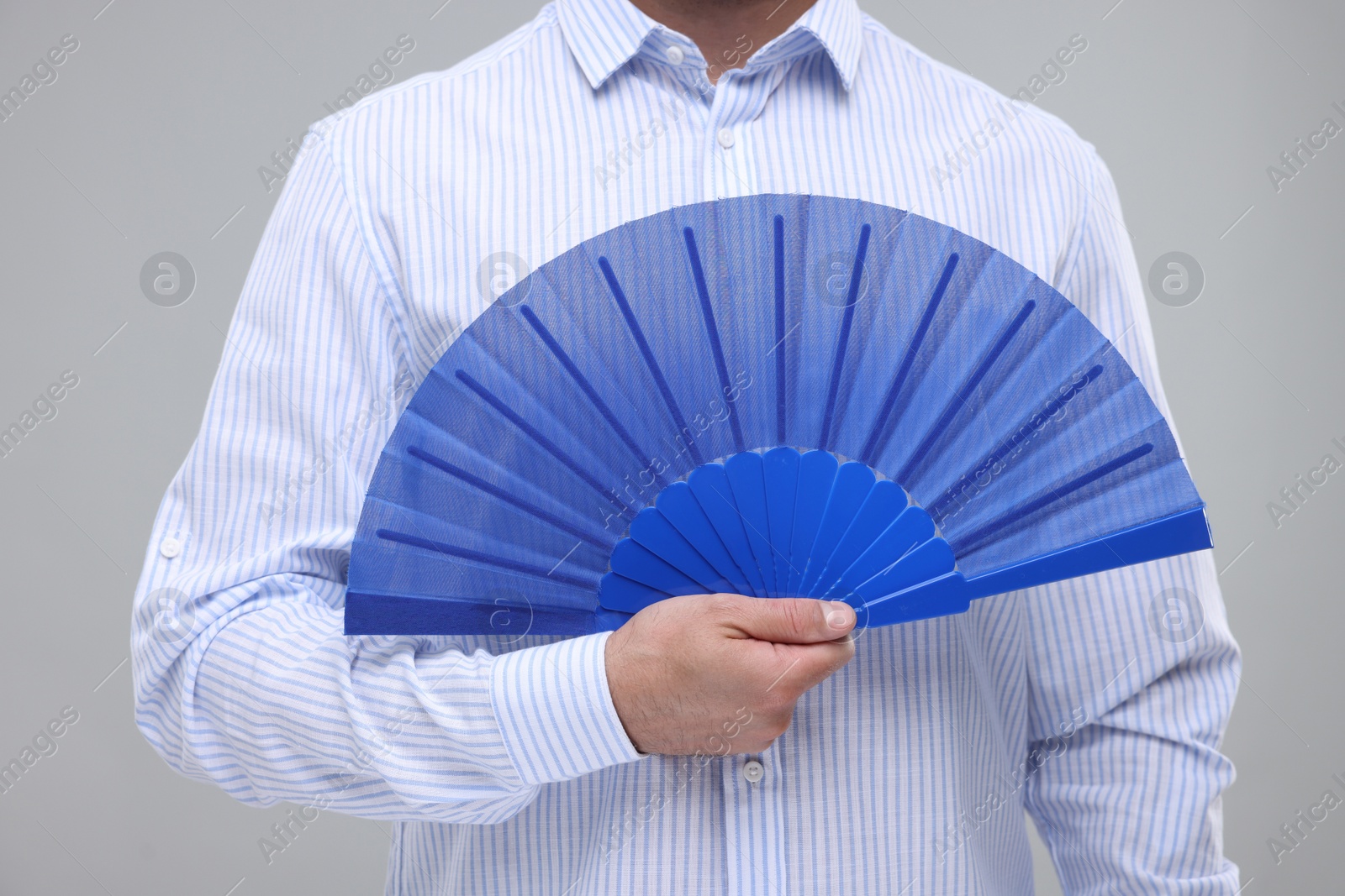 Photo of Man holding hand fan on light grey background, closeup