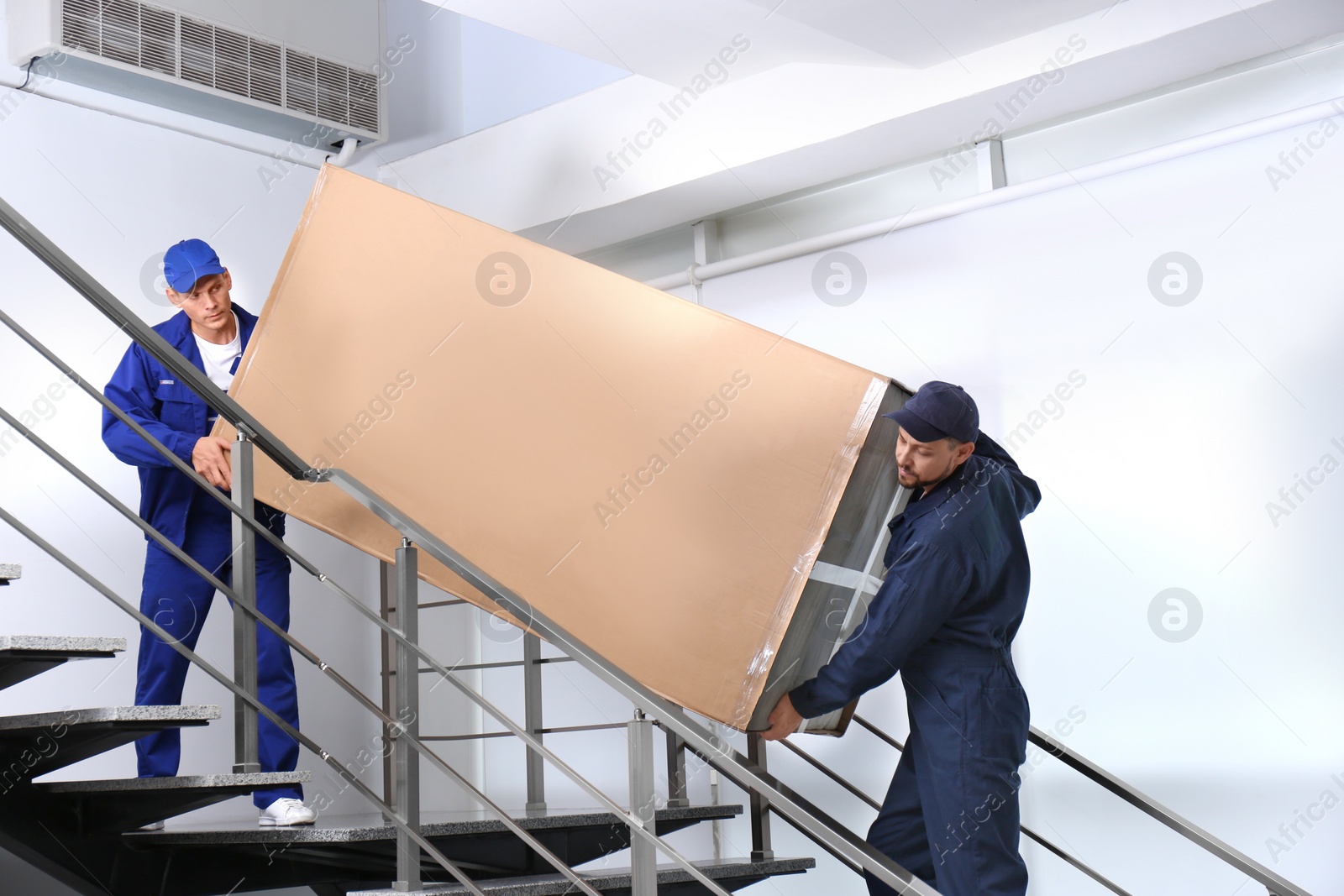 Photo of Professional workers carrying refrigerator on stairs indoors