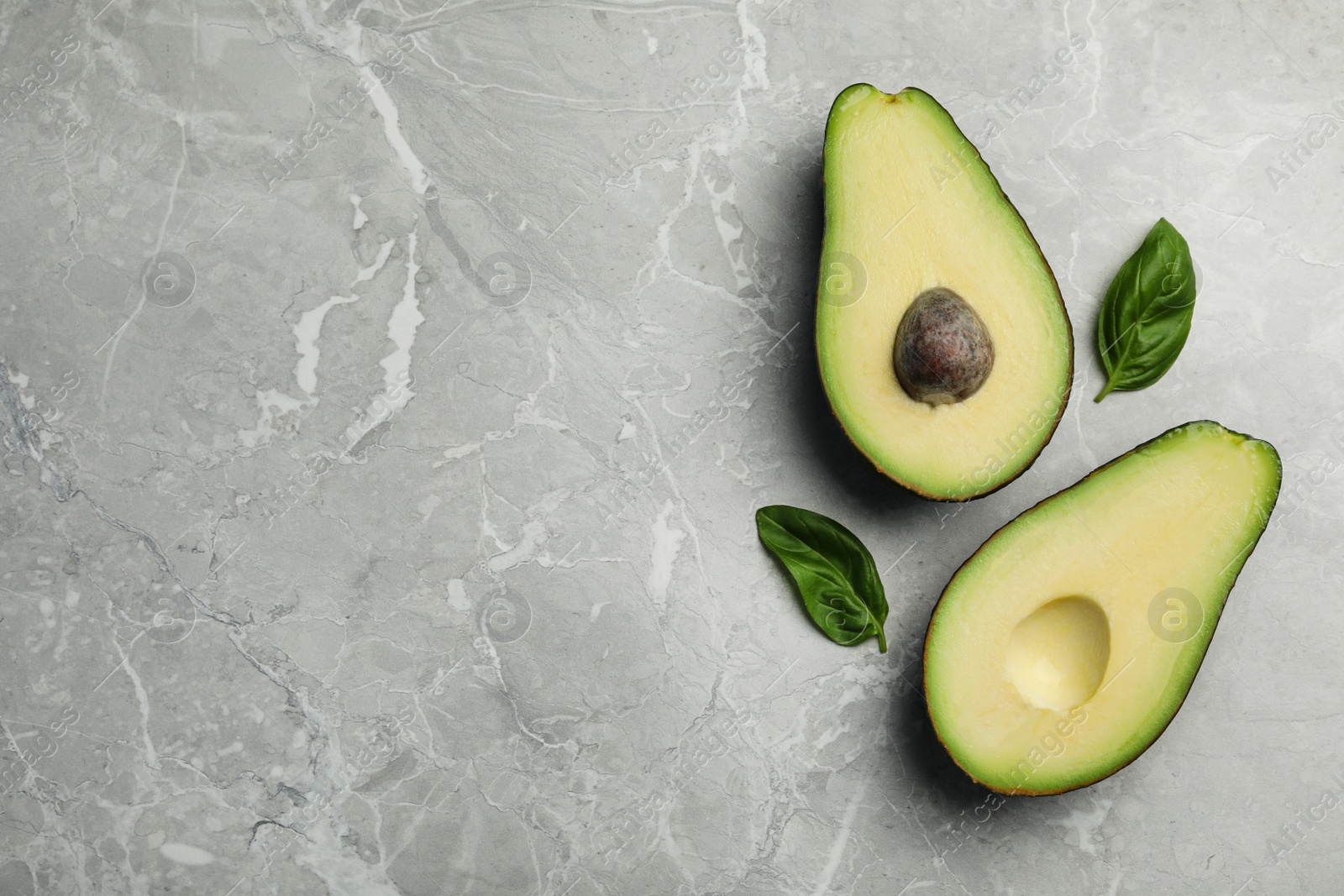 Photo of Halves of delicious ripe avocado on grey marble table, flat lay. Space for text