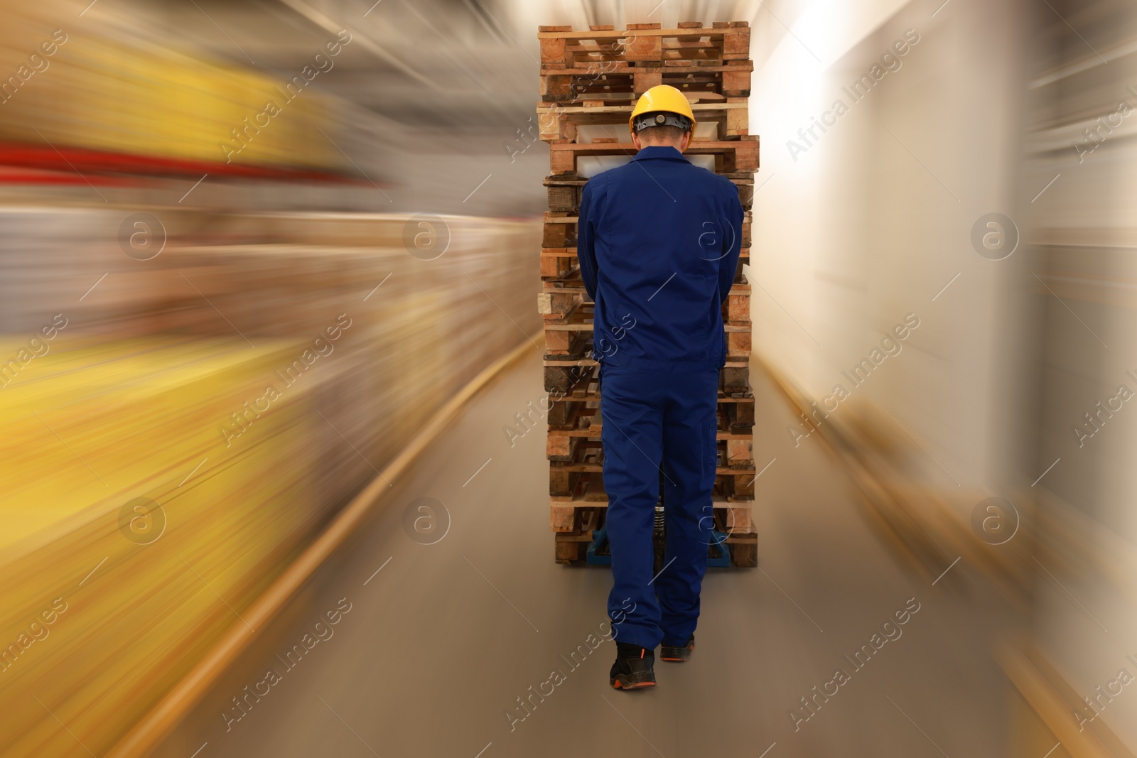 Image of Worker moving wooden pallets with manual forklift in warehouse, back view