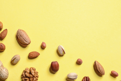 Photo of Different delicious nuts on yellow background, flat lay. Space for text