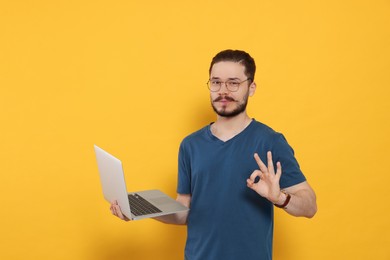 Handsome man with laptop showing OK gesture on orange background