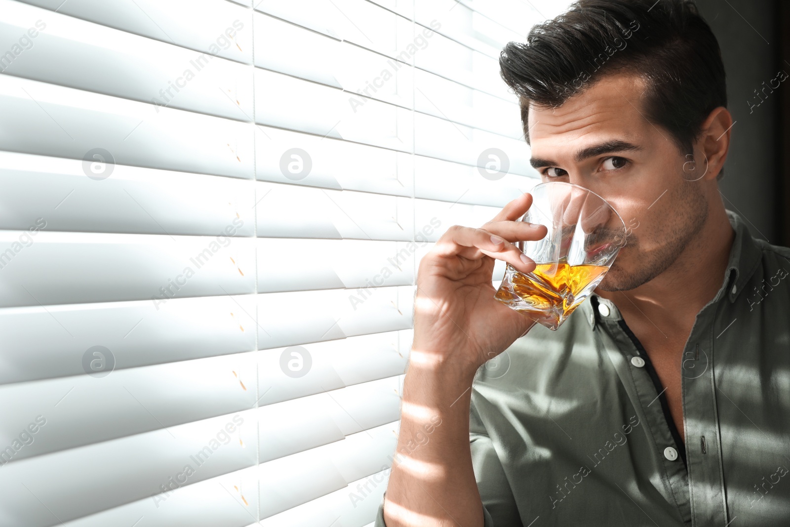 Photo of Young man with glass of whiskey near window indoors. Space for text