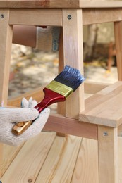 Photo of Man varnishing wooden step stool at table outdoors, closeup