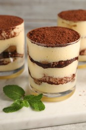 Photo of Delicious tiramisu in glasses and mint on table, closeup