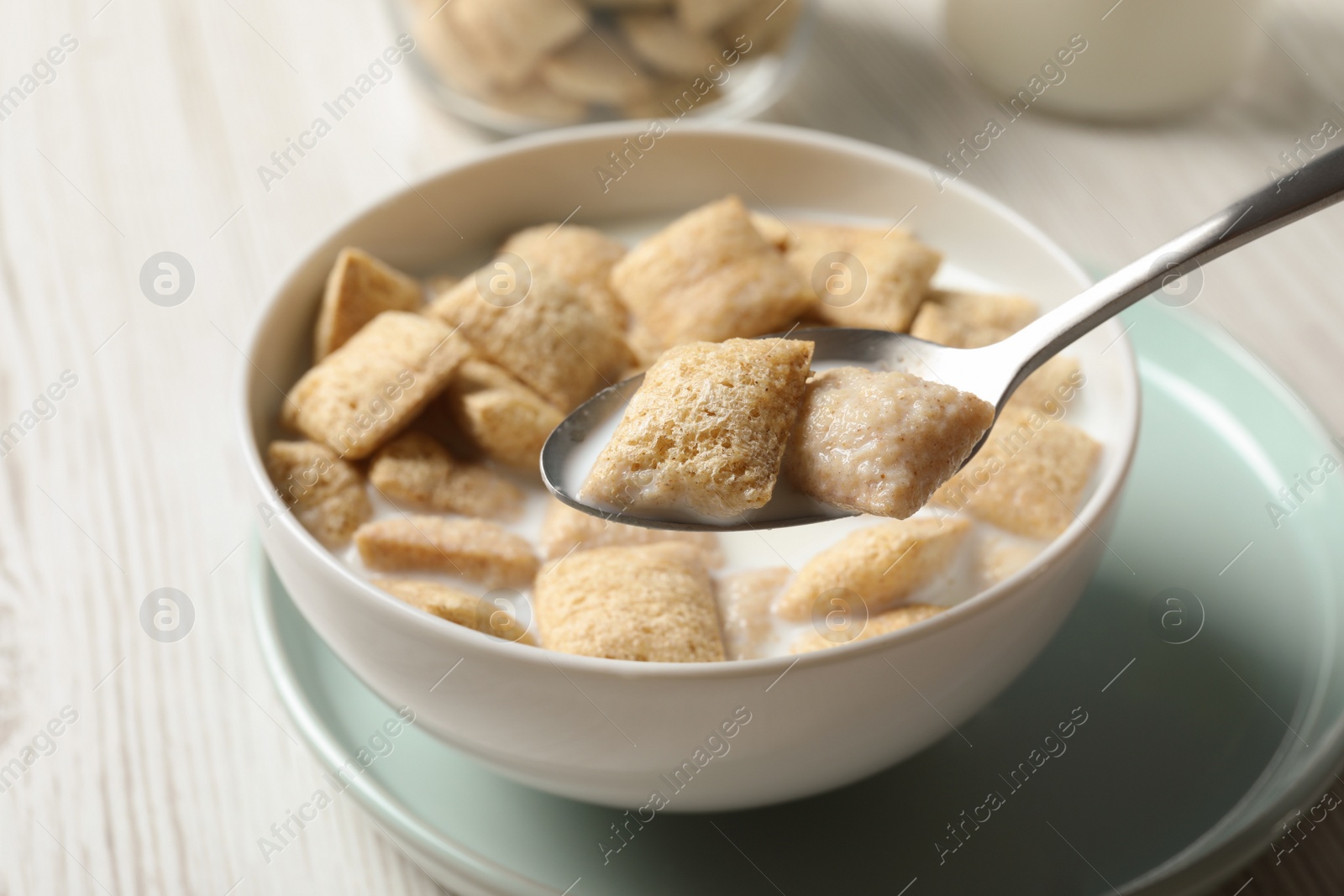 Photo of Spoon with tasty corn pads and milk over bowl on white wooden table, closeup
