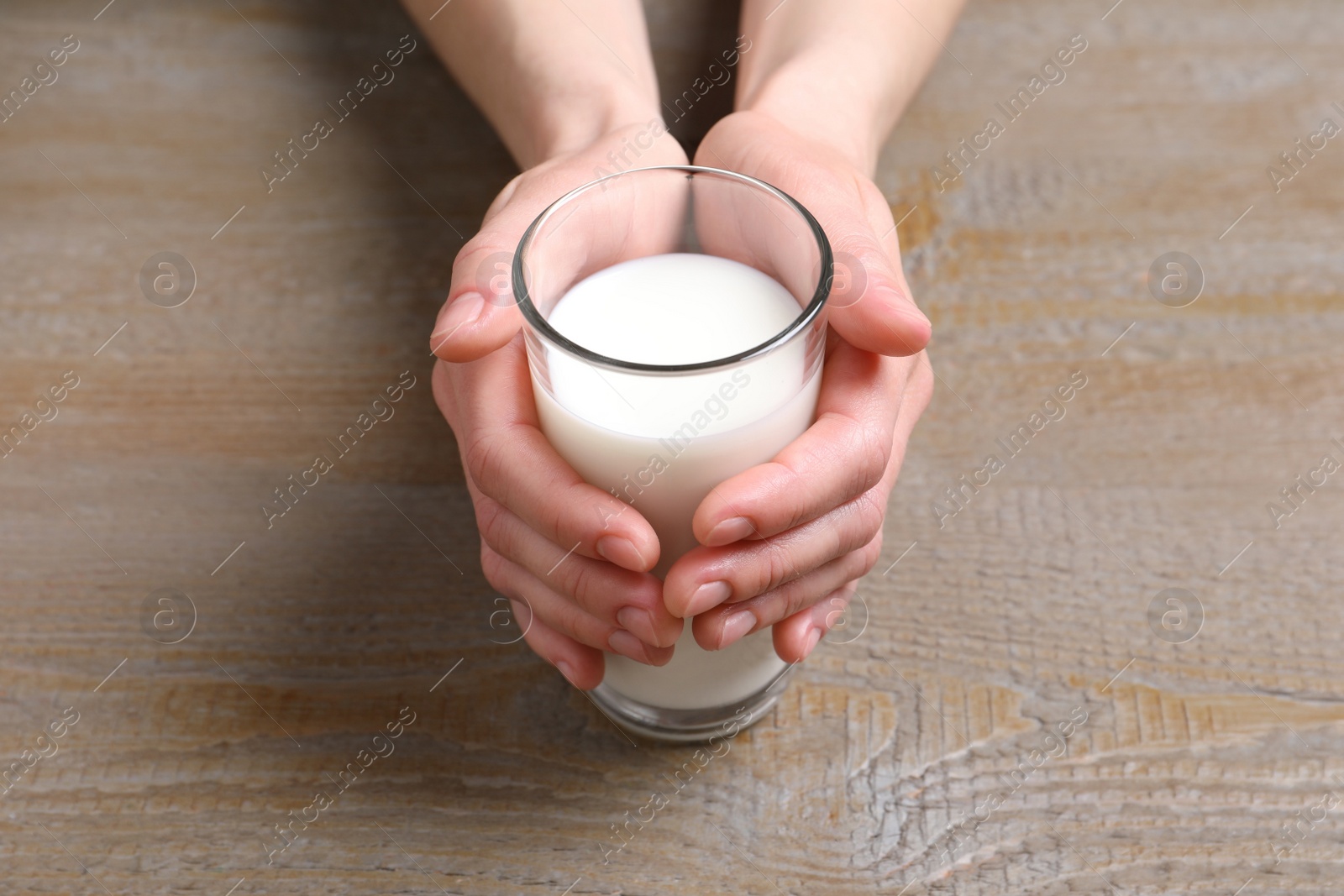 Photo of Woman holding glass of milk at wooden table, closeup