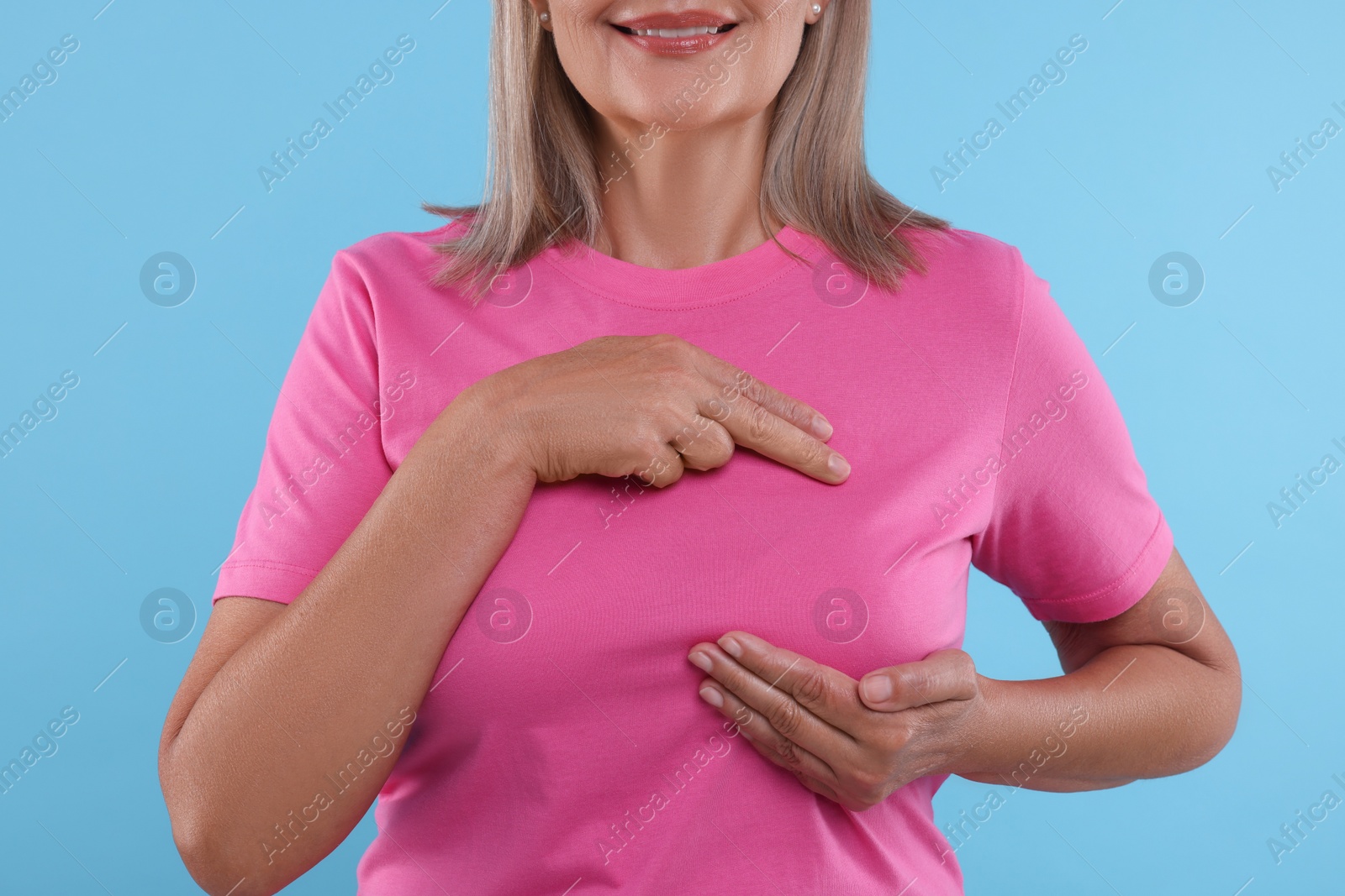 Photo of Woman doing breast self-examination on light blue background, closeup