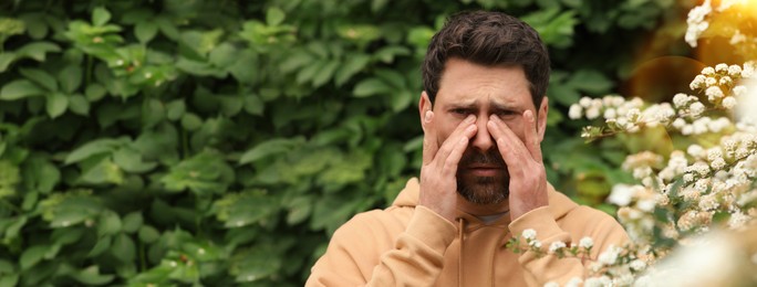 Man suffering from seasonal pollen allergy near blossoming tree on spring day. Banner design with space for text